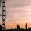 Ferris wheel and Gothic-style buildings, including Big Ben, silhouetted against a pink and orange sunset sky.