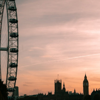 Ferris wheel and Gothic-style buildings, including Big Ben, silhouetted against a pink and orange sunset sky.