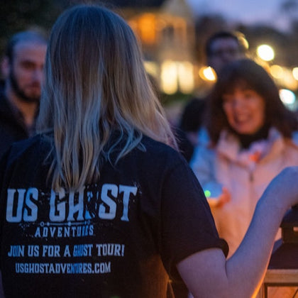 Tour guide holding a lantern as guests surround her to listen to ghost stories