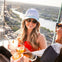 Two people toasting with cocktails on a rooftop with a cityscape and river in the background.