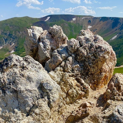 Jagged rock formations in the foreground with green hills and a blue sky in the background.