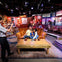 A family of three poses on an orange sofa in a colorful cafe set while a person takes their photo.