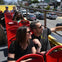 People seated on an open-top tour bus, wearing sunglasses and enjoying the view on a sunny day.