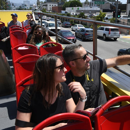 People seated on an open-top tour bus, wearing sunglasses and enjoying the view on a sunny day.