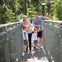 A family of four walking together on a metal bridge surrounded by lush greenery.