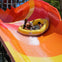 Three people riding a yellow inflatable raft on a vibrant orange and red water slide.