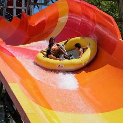 Three people riding a yellow inflatable raft on a vibrant orange and red water slide.