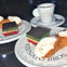 Two plates with Italian desserts, including rainbow cookies and cannoli, near a cup of espresso on a dark surface.