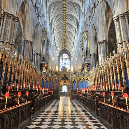 A grand cathedral interior with vaulted ceilings, ornate decorations, and a checkered floor leading to a stained glass window.