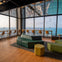 Modern lounge area with modular seating, barstools along tall windows overlooking a cityscape and waterfront view.