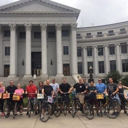 A group of people with bicycles standing in front of a large classical-style building with columns.
