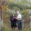 Three people stand together in a vineyard; one man gestures while the others listen. Autumn leaves and grapevines surround them.