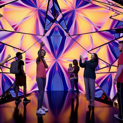 A group of people interacts with a colorful kaleidoscopic display in a modern, reflective environment.