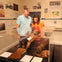 Two people observe historical sports memorabilia displayed in a museum exhibit, including gloves, a bat, and documents.