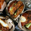 Close-up of several fried chicken sandwiches wrapped in paper, served on pretzel buns with sauce and pickles.