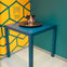 A person appears to have only their head visible on a blue table, surrounded by a yellow and teal geometric background.