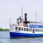 A white and blue tour boat named Oriole cruises on a calm body of water under a cloudy sky.