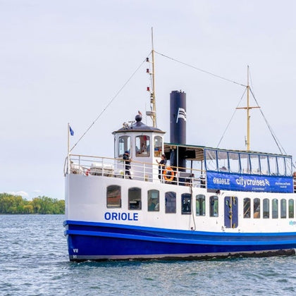 A white and blue tour boat named Oriole cruises on a calm body of water under a cloudy sky.