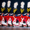 Five performers dressed as toy soldiers in red, white, and black costumes with large hats, sitting in a synchronized pose on stage.