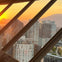 View of a city skyline with modern buildings at sunset, seen through angled window frames.