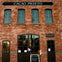A brick building with the sign 'Cacao Prieto' and a chalkboard outside featuring flags and text about bean-to-bar chocolate.