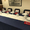 Table set with white and blue linens, plates, cups, silverware, and red napkins. Chairs feature framed Time magazine covers.
