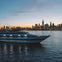 A large yacht on water with a lit-up city skyline and sunset in the background.