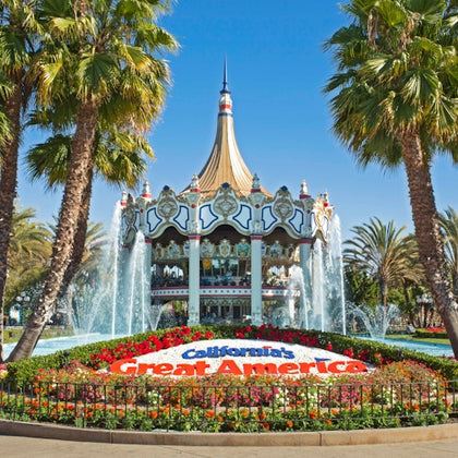 A carousel with ornate decorations surrounded by fountains and flowers, with a sign reading "California's Great America."