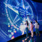 Three people interact with a large illuminated touchscreen displaying colorful graphics and Japanese text in a dark room.