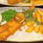 A plate with battered fish, lemon slice, peas, chips, and garnish on a light ceramic dish.