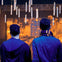 Two people with curly hair, seen from behind, facing a room with floating candles and a warm, glowing ambiance.