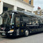 Black tour bus parked on a city street with "London - Bicester Village" and other text advertising a travel service on its side.