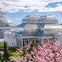 A glass greenhouse structure surrounded by blooming cherry blossoms under a sunny sky.