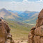 A mountain valley view framed by large rock formations in the foreground under a partly cloudy sky.