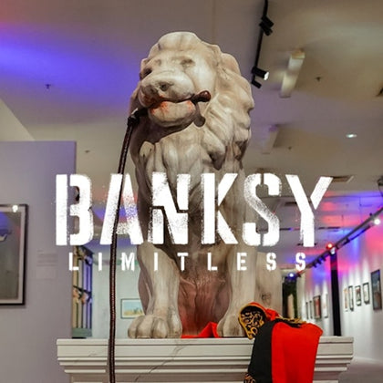 A lion statue on a pedestal displayed in an art gallery with the text 'BANKSY LIMITLESS' overlaid on the image.