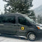 A black van with a logo parked on a snowy road, surrounded by snow-covered trees and mountains in the background.