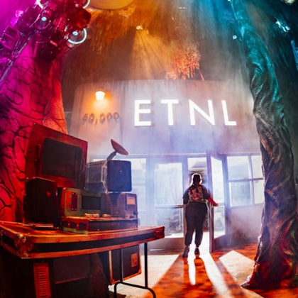A person standing in front of a building with 'ETNL' signage, surrounded by vibrant lights and retro equipment.