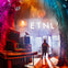 A person stands in front of a building with "ETNL" illuminated on it, surrounded by colorful lights and equipment.
