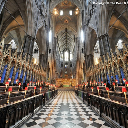 Interior of a grand cathedral with tall vaulted ceilings, ornate wooden choir stalls, and a checkered floor leading to an elaborate altar.