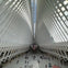 A spacious, modern interior with arched, rib-like beams, a skylight above, and people walking on the white floor below.