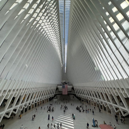 A spacious, modern interior with arched, rib-like beams, a skylight above, and people walking on the white floor below.