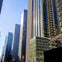 Tall modern skyscrapers reflecting sunlight with clear blue sky in the background, seen from a city street perspective.