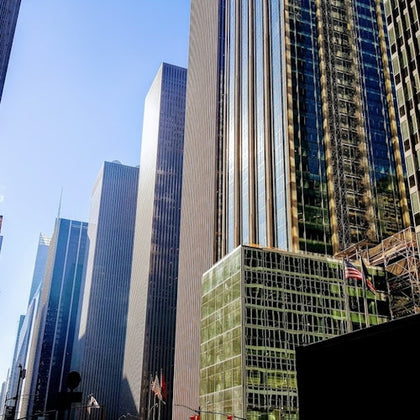 Tall modern skyscrapers reflecting sunlight with clear blue sky in the background, seen from a city street perspective.