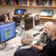 A group of people sitting at computer workstations in a library, engaged in an activity on the screens.