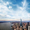 Aerial view of a cityscape featuring a prominent skyscraper, a river on the left, and a sky filled with wispy clouds.