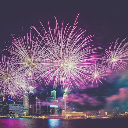 Bright fireworks illuminating a city waterfront at night with skyscrapers and reflections on the water.