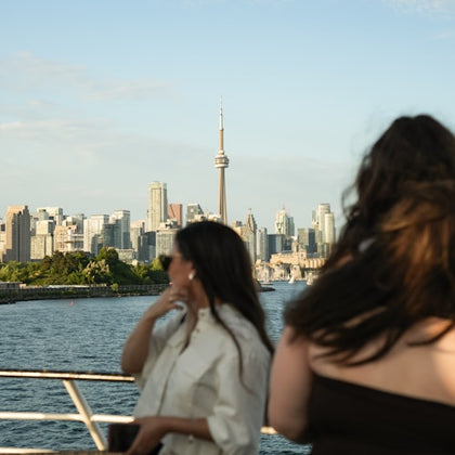 Two people on a boat with a city skyline and a tower in the background under a blue sky.