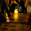 People using a Ouija board on a table with candles, letters, and numbers visible.
