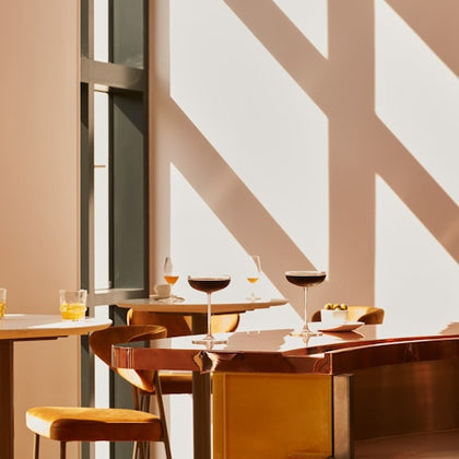 A modern dining area with tables, chairs, drinks, and sunlight casting shadows on the walls.