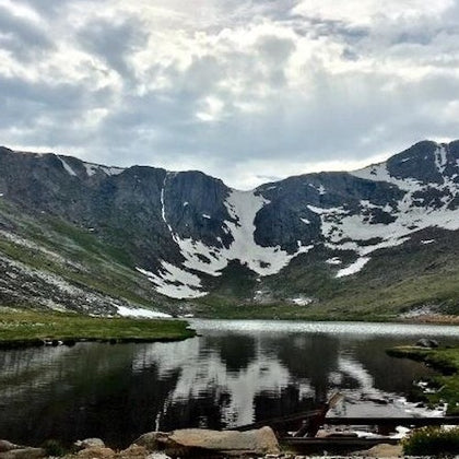 A serene alpine lake surrounded by rocky, snow-patched mountains under a partly cloudy sky.
